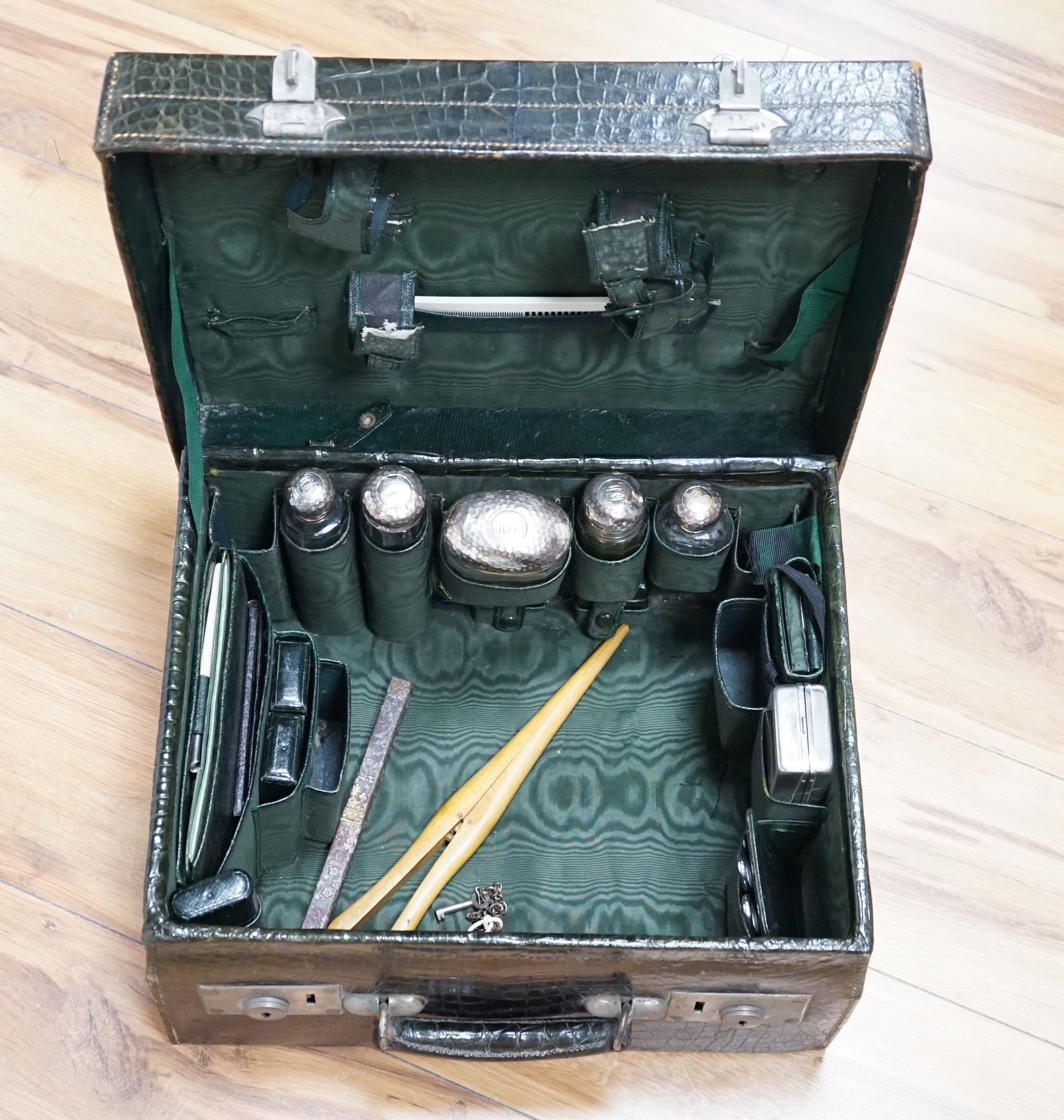 An early 20th century green crocodile toilet case with silver mounted interior, width 39 cms.